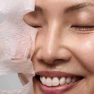 Nahaufnahme einer Person, die Lotion Mask Pads auf das Gesicht auflegt und entfernt